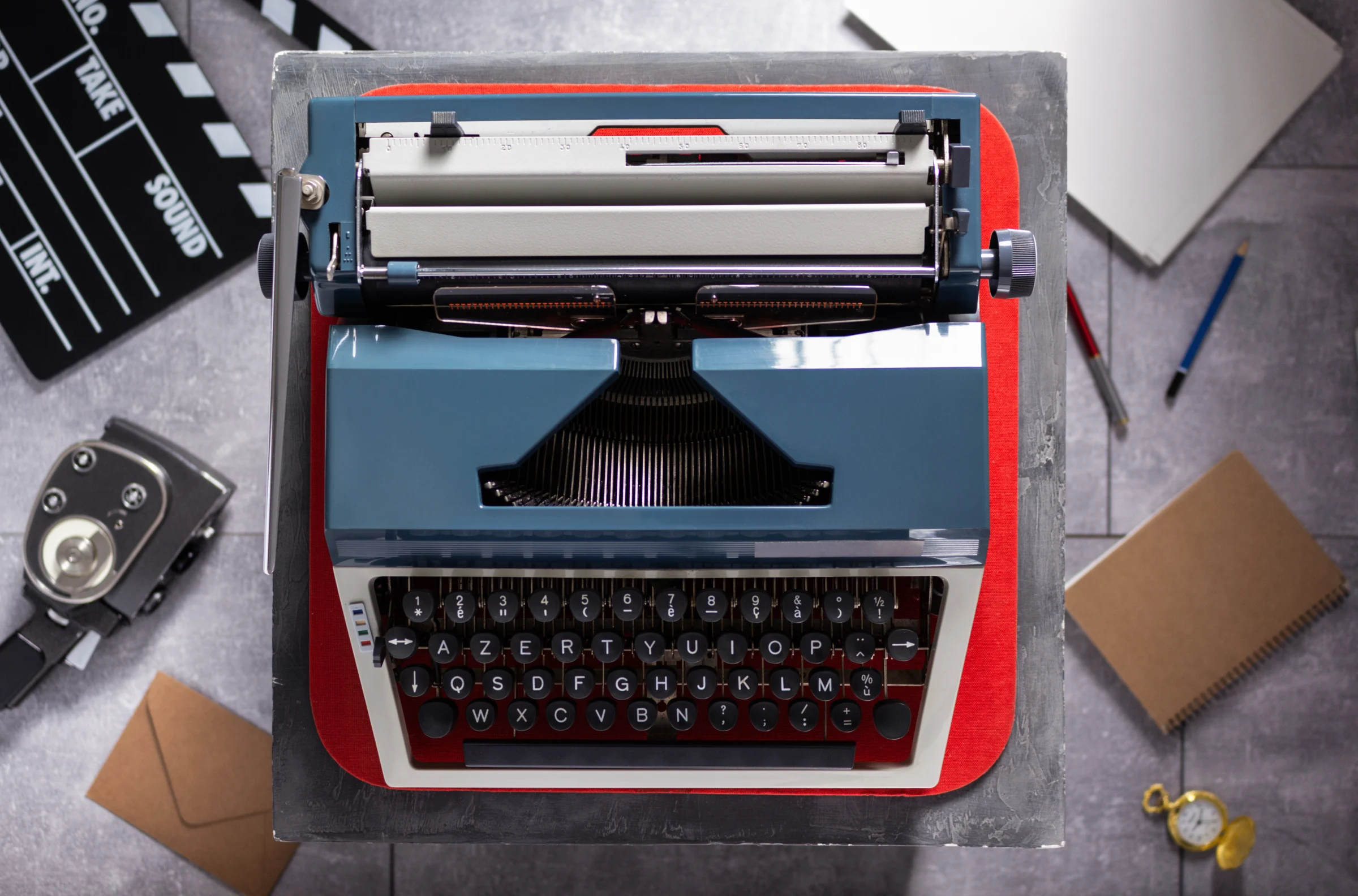 An overhead view of a vintage typewriter beside a film clapperboard and a notebook.