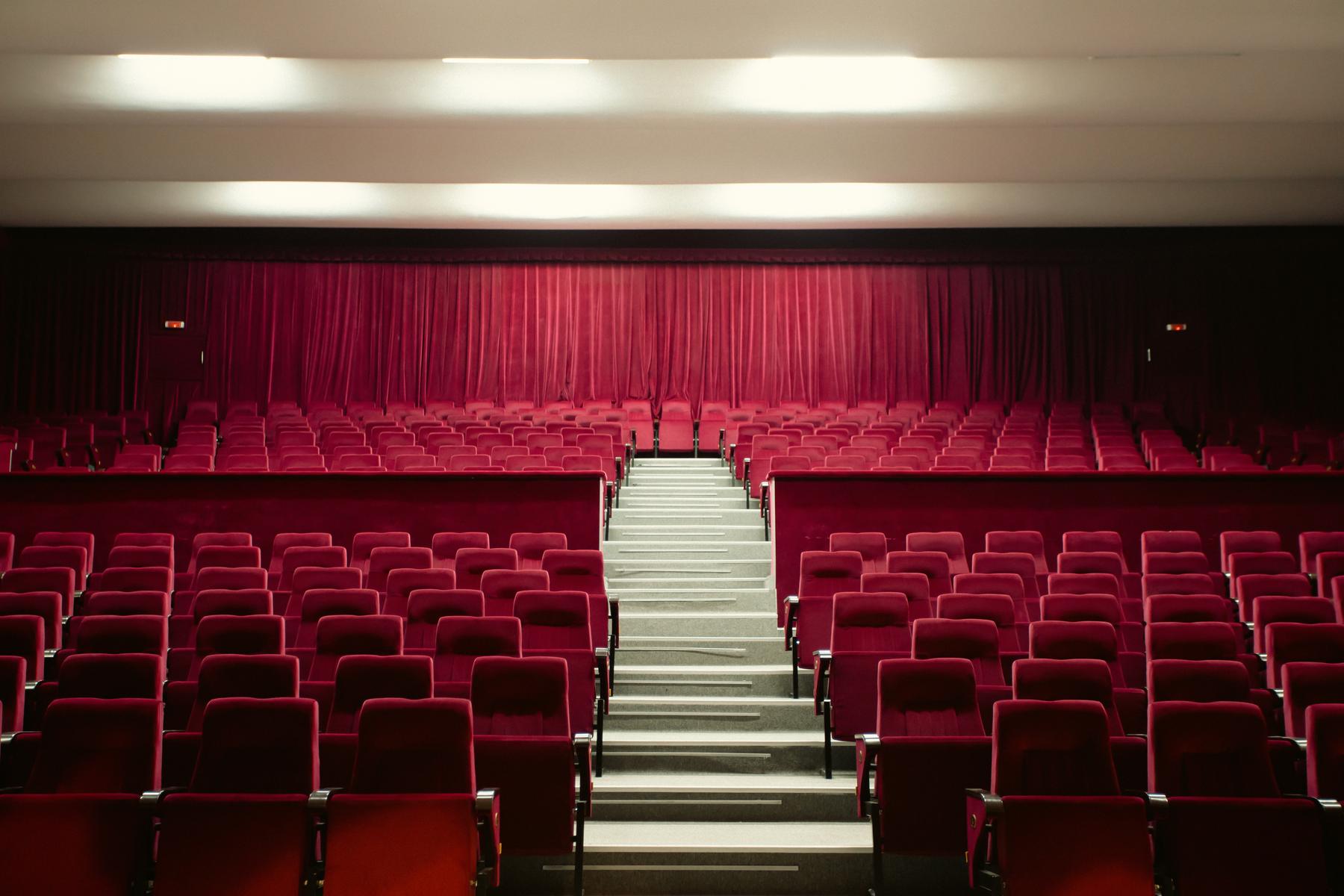 Rows of empty red theatre seats facing a lit stage.